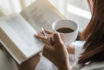 Asian,woman,holding,cup,of,coffee,and,reading,a,book