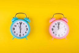 Two,alarm,clocks,on,a,bright,yellow,background,showing,different