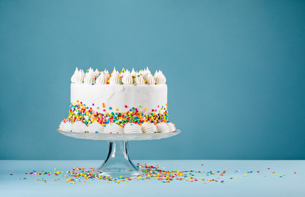 White,birthday,cake,with,colorful,sprinkles,over,a,blue,background.