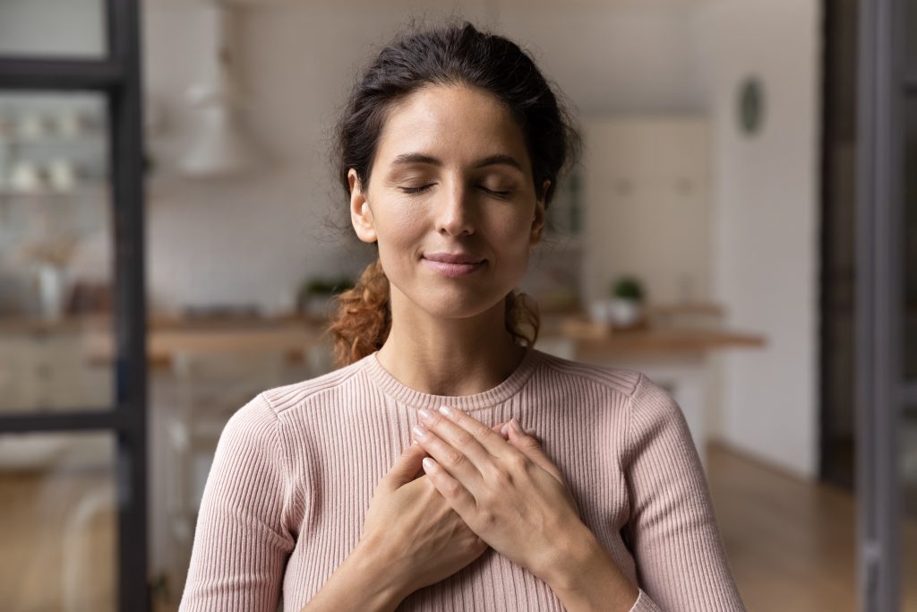 Calm Young Woman Hold Hands On Chest Praying