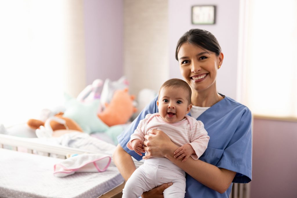Happy Nurse Carrying A Baby In The Nursery