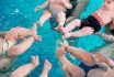 A Group Of Mothers With Their Young Children In A Children's Swimming Class With A Coach.