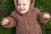 Portrait Of A One And A Half Year Old Blue Eyed Girl In A Bear Costume Lying On The Grass, View From Above