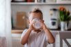 Cute Little Boy Toddler Holding Glass Drinking Milk In Kitchen At Home