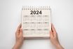 Hands Hold Calendar Year 2024 Schedule. 2024 Desk Calender Notepad On Wooden Table And Gray Background. New Year. Plans For 2024. White Background
