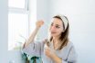 Young Woman In Bathrobe Looking In The Mirror, Holding Dropper With Hyaluronic Acid Serum Close To Face And Smiling. Skin Hydrating. Cosmetic Spa Procedures. Beauty Self Care At Home. Selective Focus.