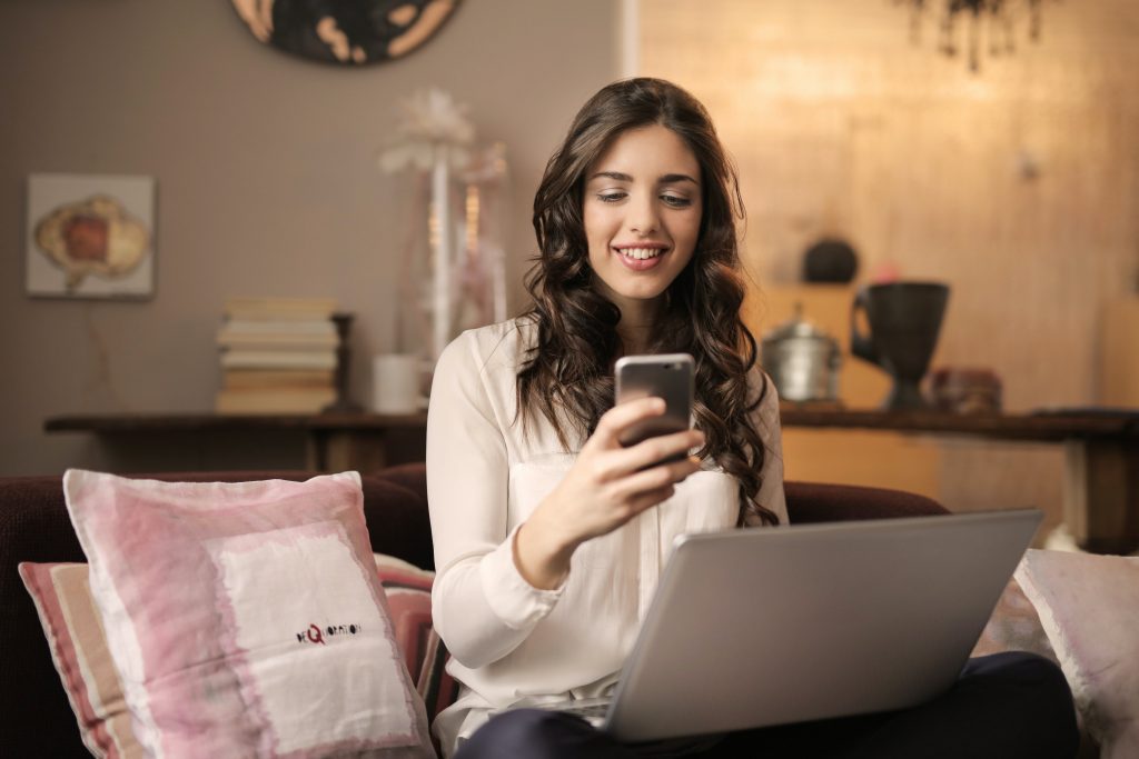 Mosolygó fiatal nő laptop előtt ülve telefonozik 