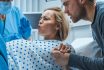 In The Hospital, Close Up On A Woman In Labor Pushing Hard To Give Birth, Obstetricians Assisting, Spouse Holds Her Hand. Modern Maternity Hospital With Professional Midwives.