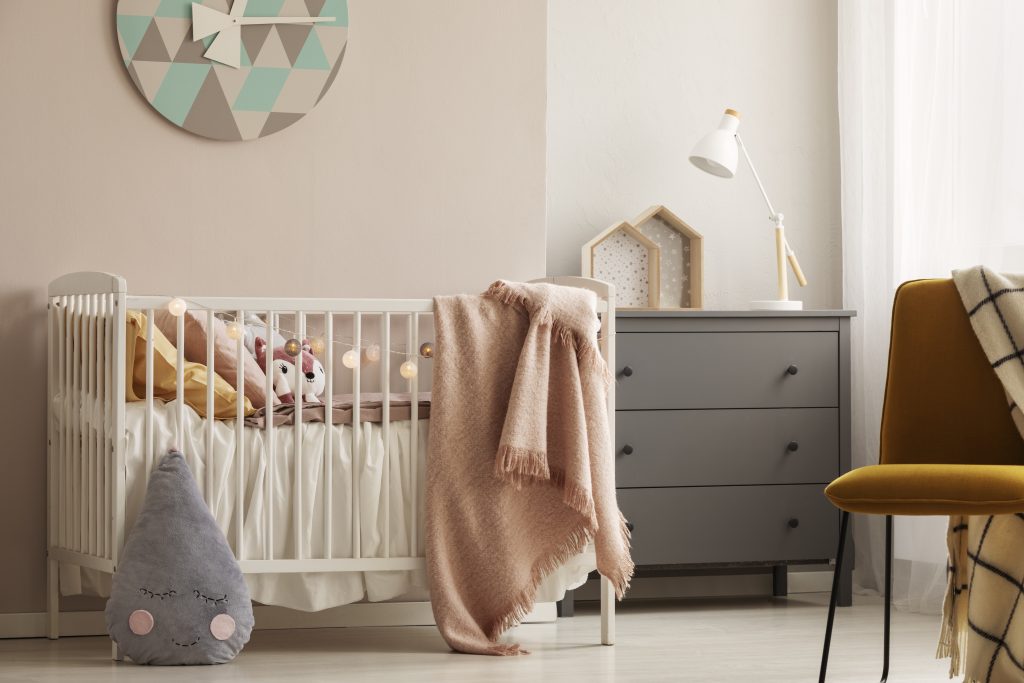 Pillows And Toy In White Wooden Crib With Pastel Pink Blanket In Bright Nursery