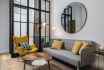 Colorful And Cozy Living Room With A Designer Armchair And Sofa Along With A Round Decorative Mirror And Glass Wall.