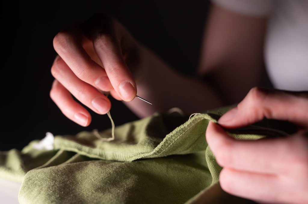 Female Hands With Sewing Needle And Thread Mending Clothes