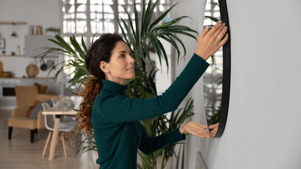 Close Up Smiling Woman Hanging Or Fixing Mirror, Decorating Apartment