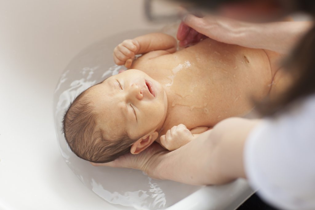 Little Baby Is Taking A Bath On The Arms Of Her Mother.