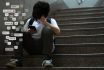 Asian Teenage Boy Sitting At Stair, Covering His Face With Hands, Face Down, Holding Smartphone In Low Light.