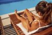 Woman Applying Sunblock While Sunbathing By The Pool