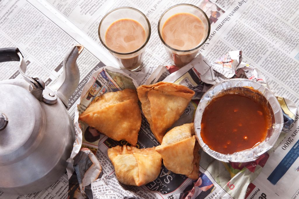 Directly Above Shot Of Samosas. Chutney And Tea On Newspaper