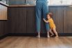 Portrait Of A Baby Girl Embracing Mother's Leg And Asking To Take Up. Baby Standing Holding Legs. Family Care. Baby Care.