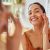 Smiling Mixed Race Young Woman Applying Moisturizer On Her Face In Bathroom