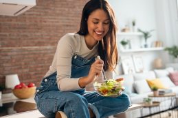 Smiling Woman Eating Healthy Salad While Sitting On The Kitchen Table At Home.