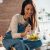 Smiling Woman Eating Healthy Salad While Sitting On The Kitchen Table At Home.