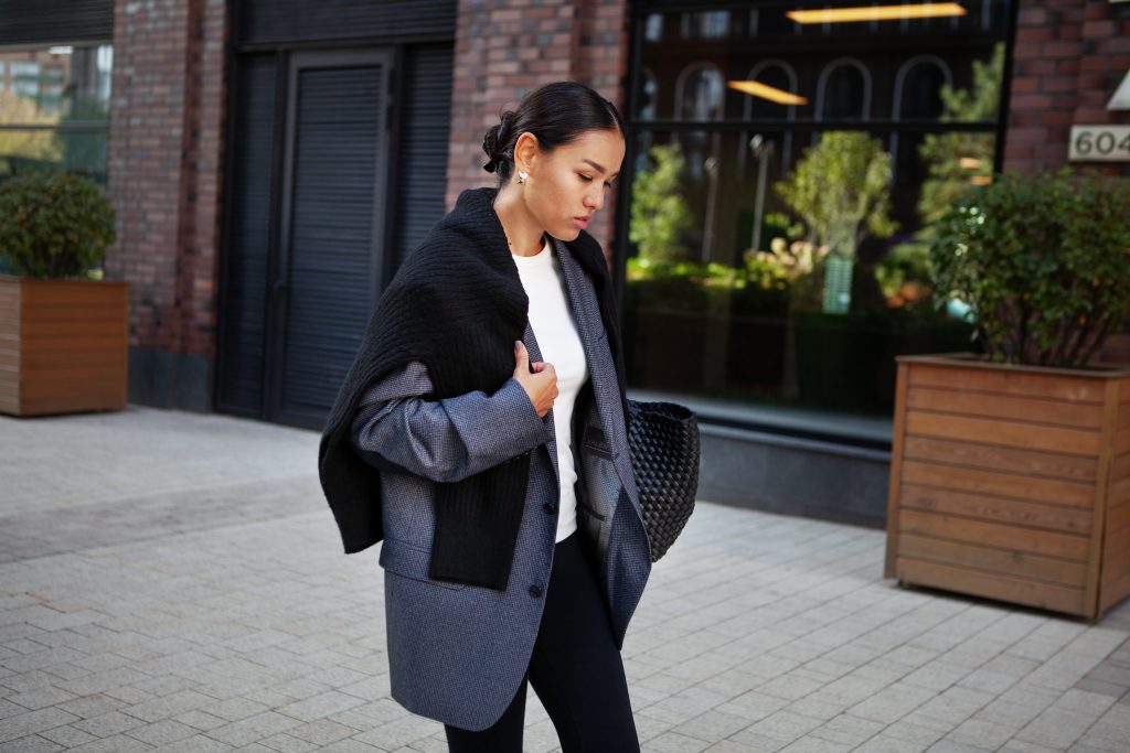 Stylish Fashion Woman Strolls Down The Street In Multilayer Clothes Oversized Blazer, Black Leggings. Fashionable Outfit, Street Style