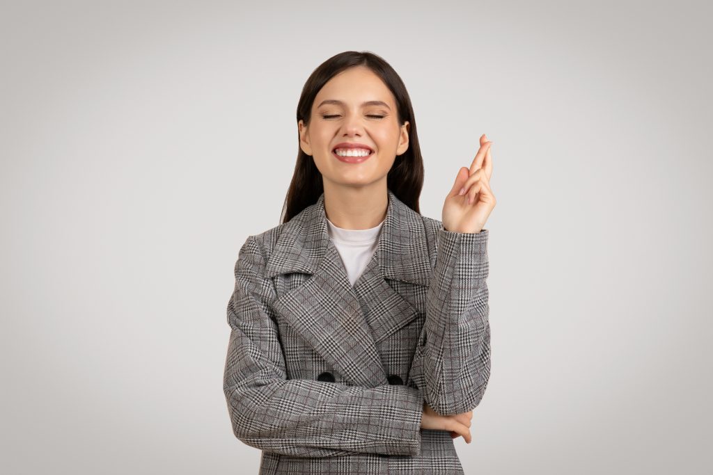 Confident Woman In Checkered Jacket Crossing Fingers With A Smile