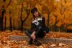 Modern Young Woman In Stylish Warm Clothes In Leather Shoes Is Resting Sitting On The Ground In The Park Among Orange Yellow Leaves In The Park. European Girl Model Enjoys An Autumn Day. Fashion.