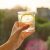 Glass Of Clear, Sparkling Water With Lemon In Hand. Background Sky, Silhouette Of The City, Sunset