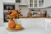 Still Life. Yellow, Orange Flowers In A Vase, Pumpkins And Candles On A Golden Tray On A White Table In A Home Kitchen Interior. A Cozy Autumn Concept.