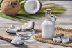 Glass Bottle Of Coconut Oil And Fresh Coconut Fruit On Wooden Rustic White Background