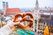 Hand With Pretzel On The Background Of The Panorama Of Munich Square, Town Hall, Christmas Fair. Germany In Winter.