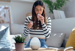 Cheerful Woman Girl Holding A Bottle Of Essential Oil While Testing It Sitting On A Couch At Home.