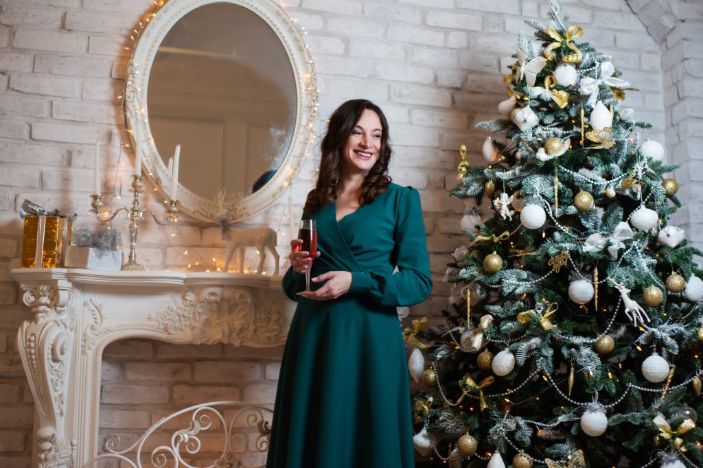 Woman In Green Dress Posing Near The Christmas Tree And Fireplace