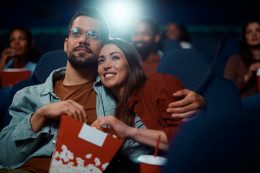 Young Couple Eating Popcorn While Watching Movie In Cinema.