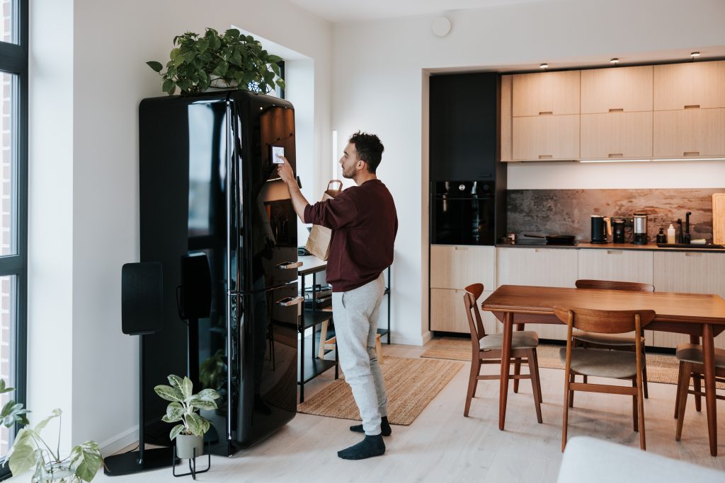 Man Interacts With His Smart Fridge, Holding A Bag Filled With Fresh Groceries