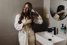 Woman Combing Her Beautiful Hair With Brush While Standing Near Mirror In Bathroom