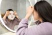 Woman Applying Facial Mask In Modern Bathroom Mirror