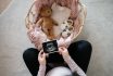 Overhead View Of Asian Pregnant Woman Holding An Ultrasound Scan Photo Of Her Baby, With A Moses Basket Filling With Baby Clothing, Baby Shoes And Soft Toy Teddy Bear In Front Of Her. Mother To Be. Expecting A New Life. Preparing For The New Born Concept