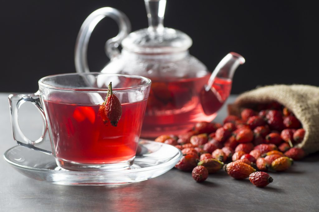 Dried Rose Hip Glass Cup Of Herbal Tea Medicinal Plants With Rosehip Fruits In Burlap Sack And Glass Teapot On Black Rustic Table