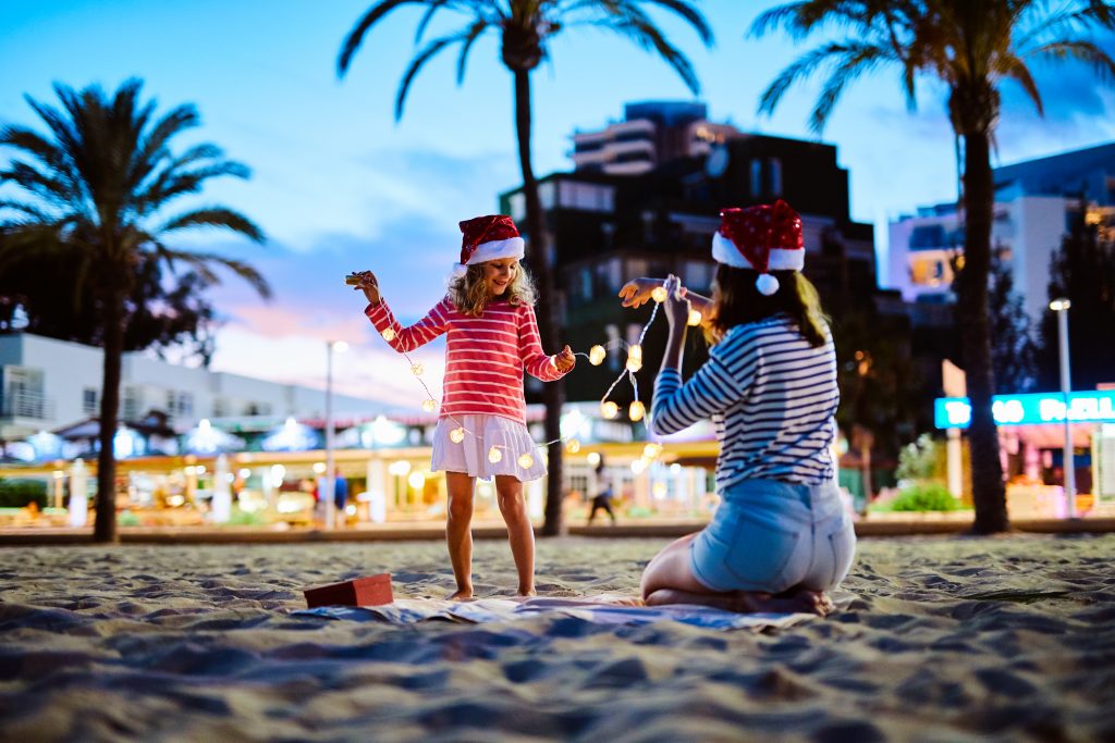 Mother And Daughter Playing With Christmas Lights On The Beach