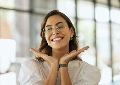 Cheerful Business Woman With Glasses Posing With Her Hands Under Her Face Showing Her Smile In An Office. Playful Hispanic Female Entrepreneur Looking Happy And Excited At Workplace