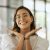 Cheerful Business Woman With Glasses Posing With Her Hands Under Her Face Showing Her Smile In An Office. Playful Hispanic Female Entrepreneur Looking Happy And Excited At Workplace