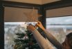 Young Woman Placing A Shiny Decorative Star On The Top Of The Christmas Tree.