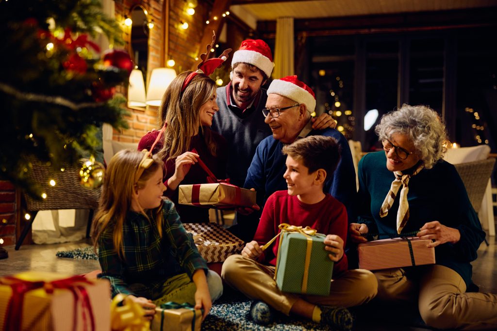 Happy Extended Family Opening Presents By Christmas Tree At Home.