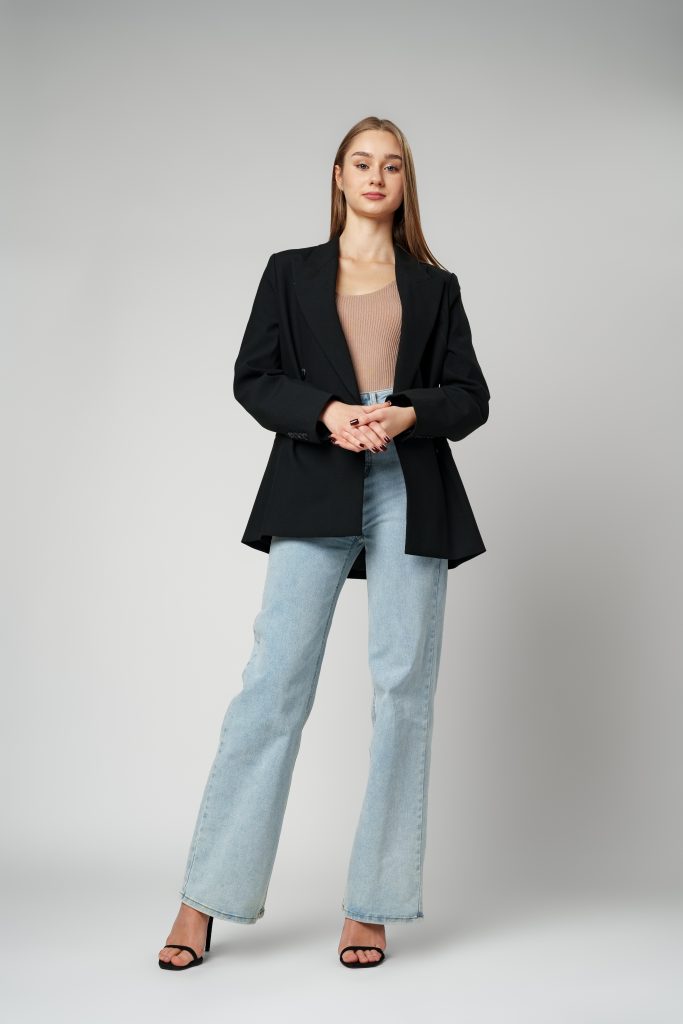 Young Woman Wearing Black Jacket And Jeans Posing On Gray Background Studio Shot .