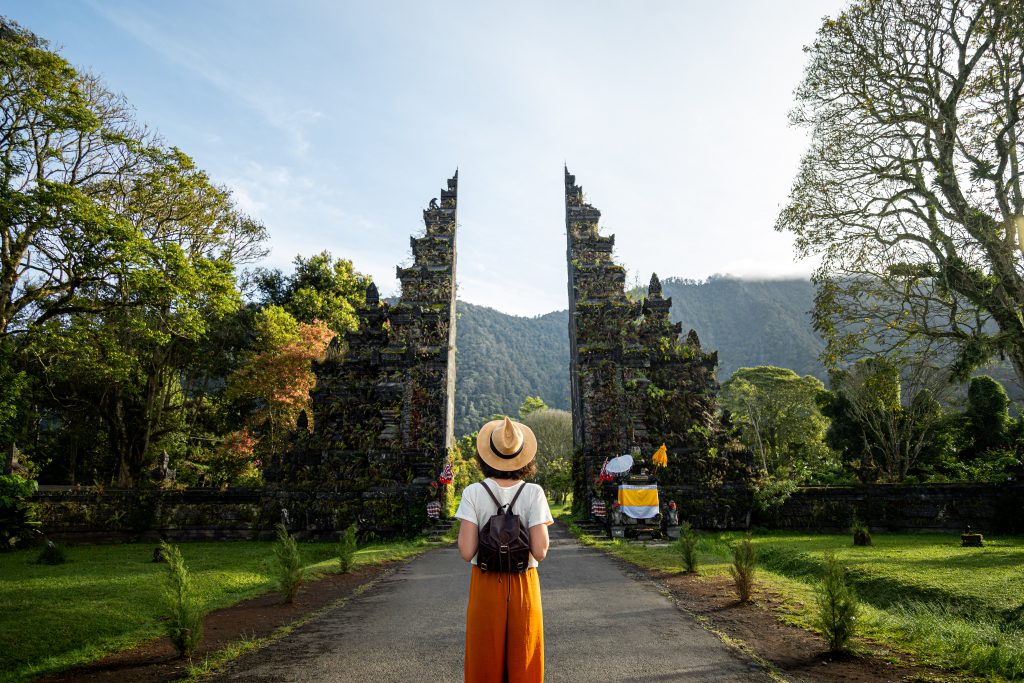 Woman Traveler With Backpack Enjoying Balinese Hindu Temple Entrance. Female Tourist During Holidays. Copy Space.