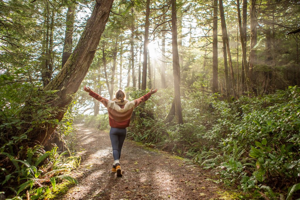 Young Woman Embracing Rainforest Standing In Sunbeams Illuminating The Trees