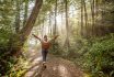 Young Woman Embracing Rainforest Standing In Sunbeams Illuminating The Trees