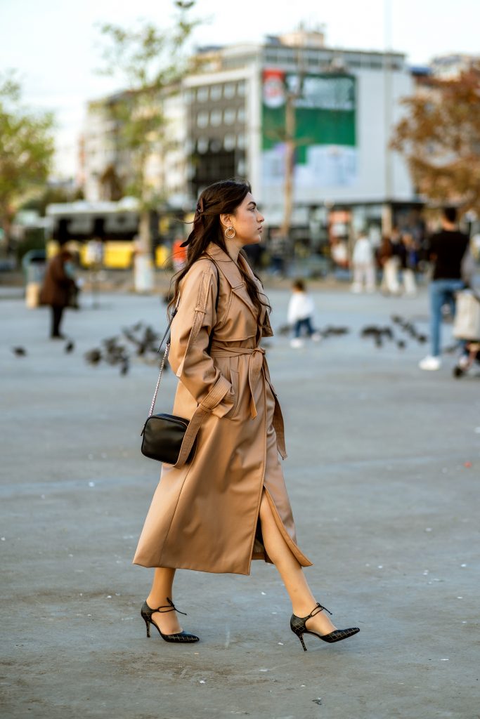 Young Woman Walking On Crowded Street In Trench Coat In Autumn