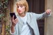 A Young Woman With Blond Hair Looks At Her Cell Phone Expressing Anticipation And Concern